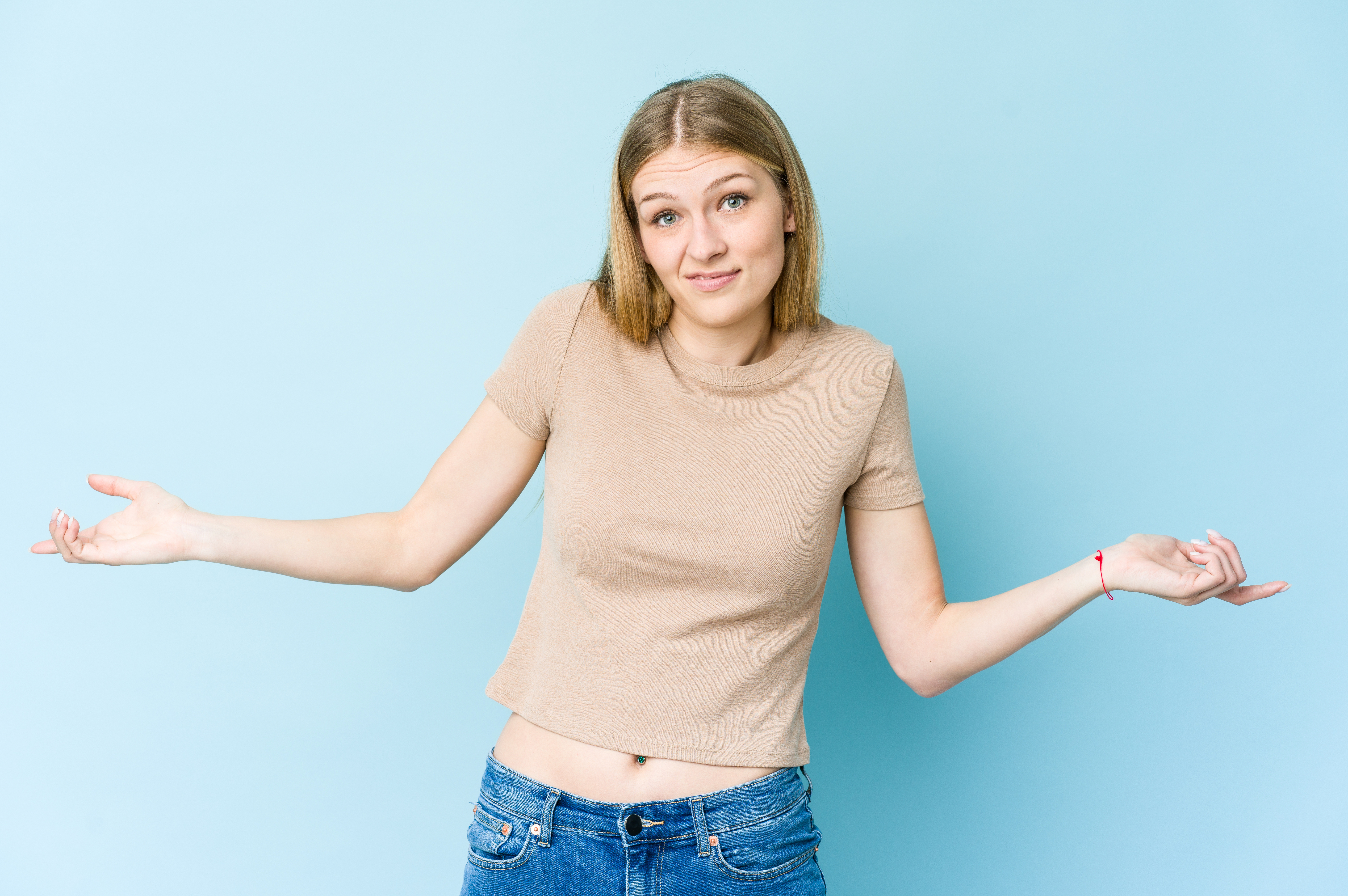Young blonde woman isolated on blue background doubting and shrugging shoulders in questioning gesture.